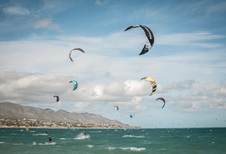 Eight people practicing kitesurf in La Ventana BCS Mexico with colorful kites and the mountains behind.