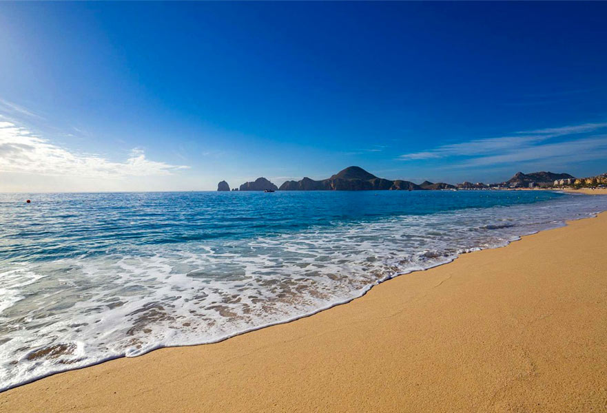 Medano beach seashore with beautiful blue turquoise water waves and The Arc mountains on the distance, Los Cabos, Mexico.