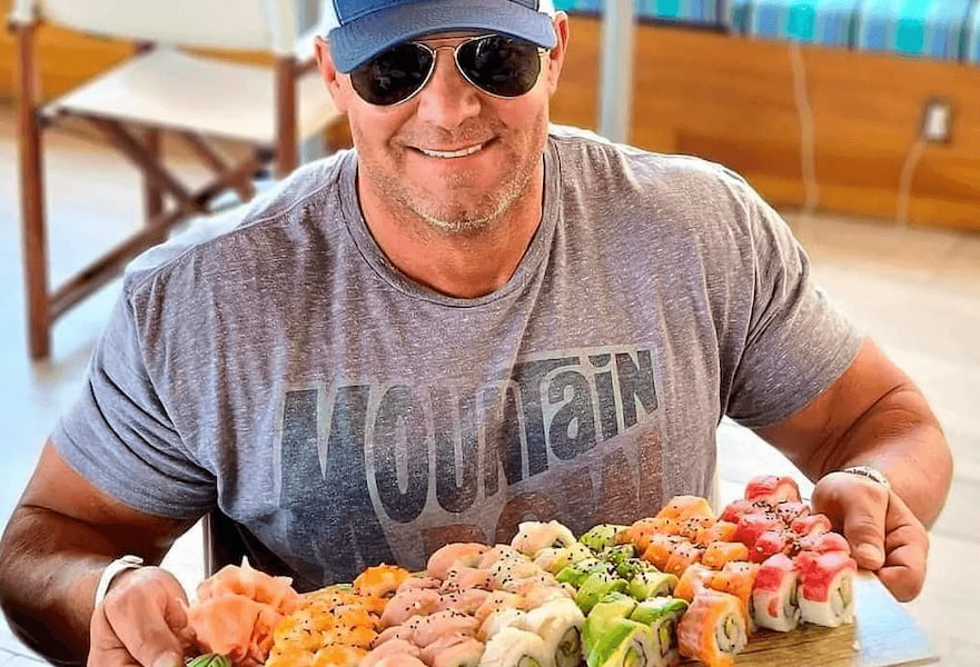 Male tourist with cap and sunglasses holding a sushi tray at Aleta Restaurant in Cabo San Lucas, Mexico.