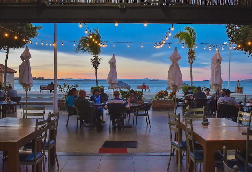 Outdoor seating area with ocean view and two groups of people eating at Bismark-cito restaurant in La Paz, Mexico.