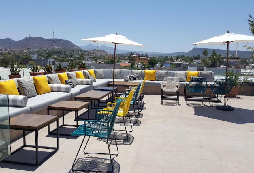 Roof terrace of Hotel Catedral La Paz, with yellow and grey cushions, two shades, and colorful Mexican chairs.