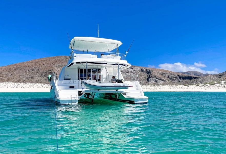 White luxury medium-sized boat on the turquoise waters of La Paz beaches, with white sand and low hills on the back.