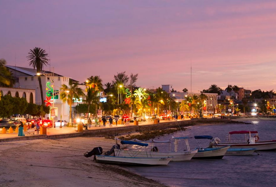 La Paz, Mexico, promenade or Malecon during the sunset with purple skies, city lights, and five boats stranded on the seashore.