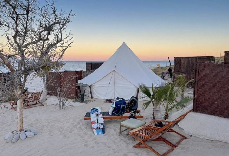 White glamping tent with two sun loungers, two backpacks, and a desert tree in La Ventana BCS, Mexico.
