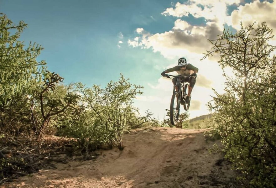 A male practicing mountain biking on a dusty road with desert plants and clear blue skies in La Ventana BCS, Mexico.