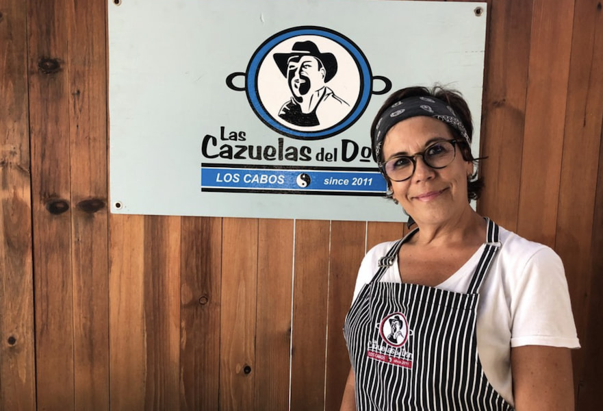 Woman who is owner of Las Cazuelas del Don posing next to the signboard