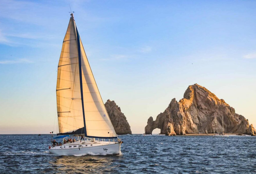 Sailboat sailing at the sunset near The Arc rock formation in Cabo San Lucas, Mexico.
