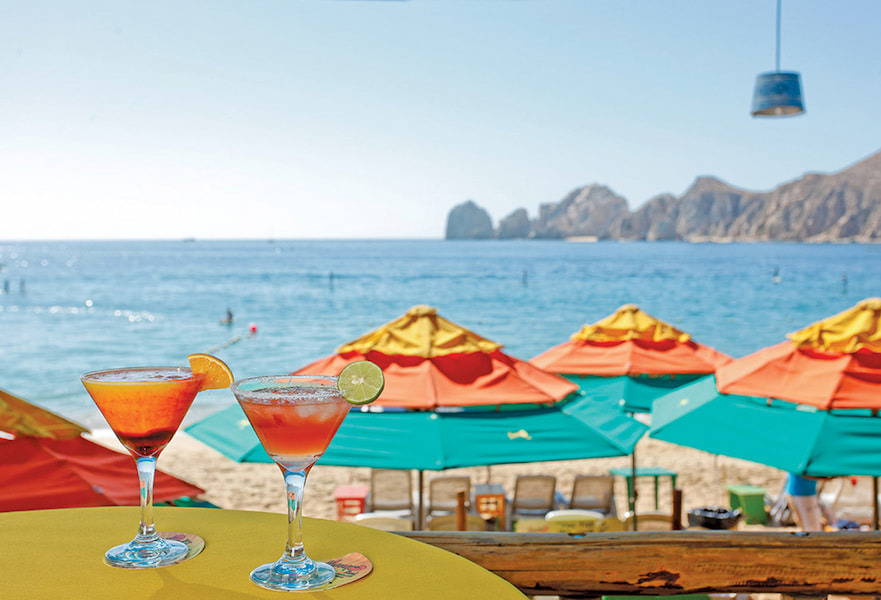 Mango Deck table with two martinis overlooking to the beach club in front of Medano Beach in Cabo San Lucas, Mexico.