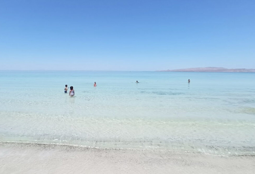 Playa escondida with clear blue skies, transparent waters and white sand with five people swimming there.