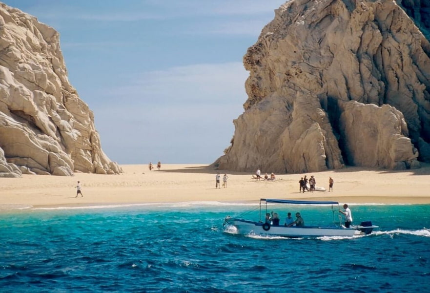 Water taxi arriving at the seashore of Lover's beach while people walk on the sand in Cabo San Lucas, Mexico.