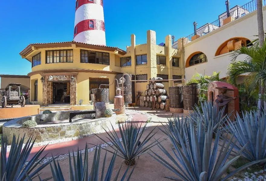 External view of Tequila Lighthouse building with wooden barrels and agave plants in the floor in Cabo San Lucas, Mexico.