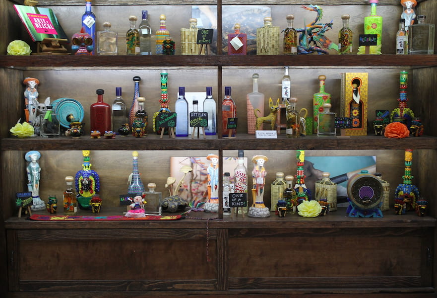 Dozens of tequila bottles with different shapes, sizes and colors, mixed with Mexica deco art in Tequila Lighthouse, Mexico.