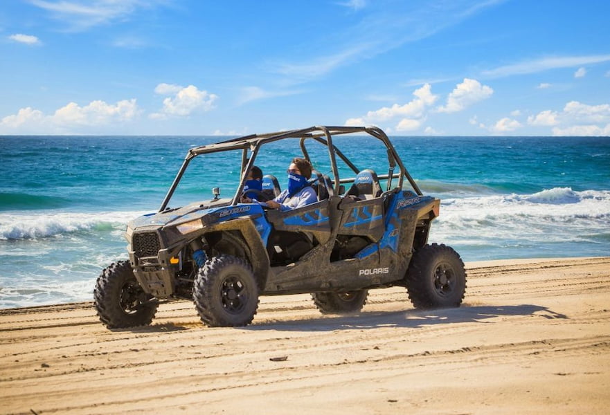 All terrain vehicle running along the beach with ocean waves at the background, Cabo San Lucas, Mexico.