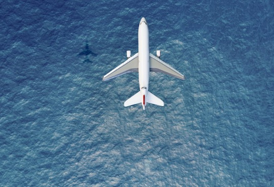 Direct flights to Cabo San Lucas, Mexico. Aerial shot of airplane overflying the deep blue ocean.