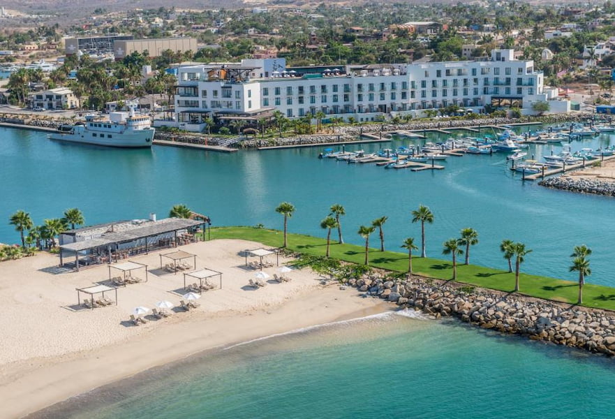 Panoramic view of Hotel El Ganzo, white building with private marina, beach club and decorative palm trees, Los Cabos, Mexico.
