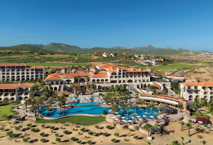 Aerial shot of Secrets Golf & Spa Resort, with poolside front-view and decorative palm trees, Los Cabos, Mexico.