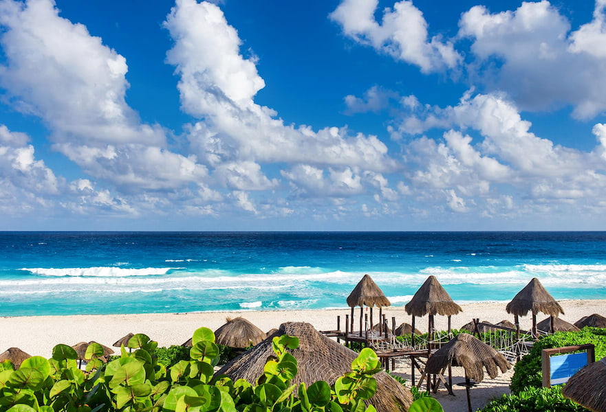Ocean view on the beach, white sand, vegetation and palapas in Cancun, Mexico